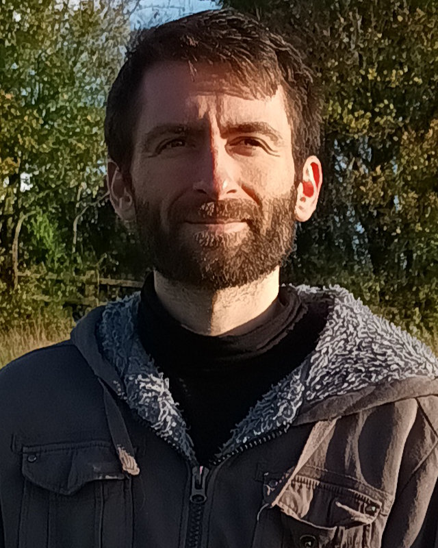 A picture of me in a field with some trees smiling at the camera.